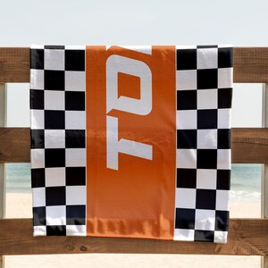 May include: A black and white checkered beach towel with an orange stripe and the word "TOTO" printed in white.
