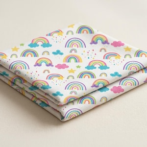 May include: Folded white fabric with a repeating pattern of colorful rainbows, clouds, stars, and sprinkles. The rainbows feature a spectrum of colors, and the clouds are pink and blue. The fabric is stacked neatly.