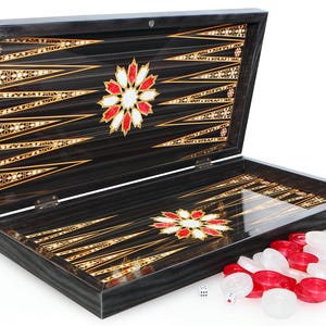 Puede incluir: Un juego de backgammon de madera con un diseño negro y dorado. El tablero de juego está abierto y las piezas están sobre la mesa. El tablero de juego tiene un diseño floral rojo y blanco en el centro.
