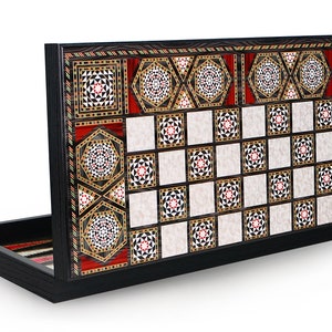 May include: A wooden game board with intricate inlaid designs in black, white, red, and gold. The board is open and shows a checkerboard pattern with a white and black background. The board is made of wood and has a black finish.