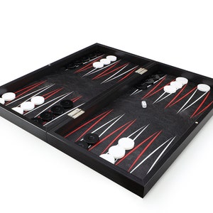 Könnte beinhalten: Ein schwarzes Backgammon-Spielbrett mit weißen und schwarzen Spielsteinen. Das Brett ist geöffnet und die Steine sind auf dem Brett angeordnet. Ein einziger weißer Würfel liegt auf dem Brett.