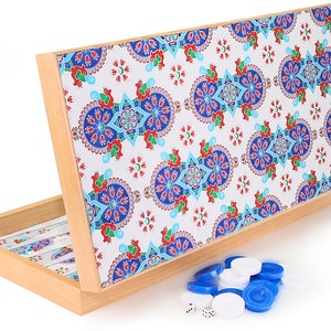 Puede incluir: Una caja de juego de madera con una tapa de diseño colorido. La caja contiene piezas de juego blancas y azules y dados.