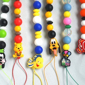 May include: Colorful beaded pacifier clips featuring cartoon characters like Goofy, Winnie the Pooh, and Nemo. Each clip has a unique bead color scheme, with characters attached to the end of the string.
