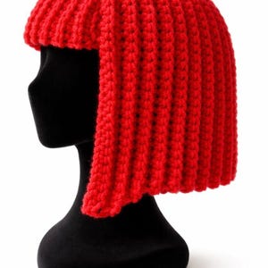 May include: A vibrant red, handmade crochet hat, styled to resemble a bob haircut. The hat is displayed on a black mannequin head, showcasing the textured, vertical ribbing of the crochet. The bright color and unique design make it a standout accessory.