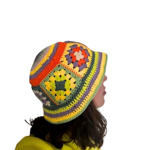 May include: A colorful crochet bucket hat featuring a patchwork design with squares and stripes in shades of orange, yellow, green, purple, and cream. The hat has a rounded crown and a short brim, perfect for sun protection.