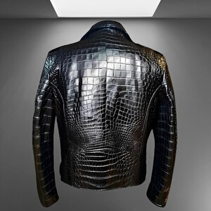 May include: A black leather jacket with a textured, crocodile-like pattern. The jacket has a classic design with a collar and long sleeves. The back of the jacket is visible, showcasing the intricate detailing of the material.
