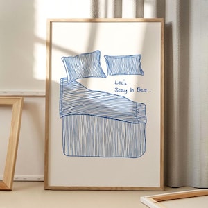 Puede incluir: Una impresión enmarcada blanca con un dibujo de línea azul de una cama con dos almohadas y el texto "Let's Stay In Bed."