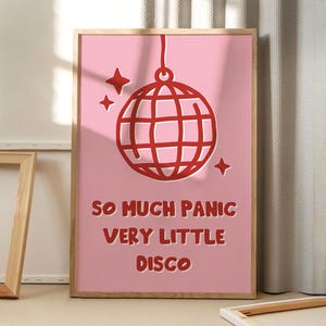 May include: A framed pink art print with a red disco ball illustration and three stars. The text reads "SO MUCH PANIC VERY LITTLE DISCO". The artwork is in a wooden frame, suitable for a bedroom or living room.