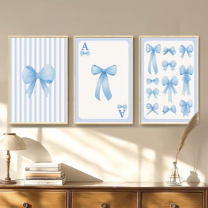 Op de afbeelding: Drie ingelijste prints met een blauw-wit gestreepte achtergrond en blauwe strikken. De middelste print toont een speelkaart met de letter 'A' en een blauwe strik. De rechter print toont meerdere blauwe strikken.