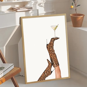 May include: A framed print of a pair of leopard print boots holding a martini glass with an olive. The boots are brown and black with a white background.