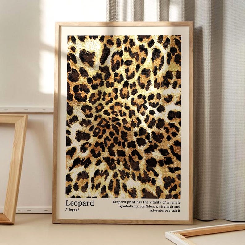 May include: A framed print featuring a leopard print pattern in shades of brown, tan, and black. The print includes the word "Leopard" and a description about the print's symbolism. The frame is a light wood color.