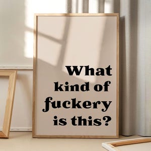 Op de afbeelding: Een beige ingelijst print met zwarte tekst die "What kind of fuckery is this?" zegt.