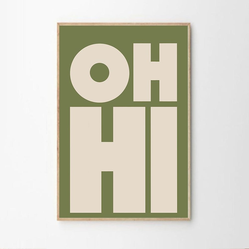May include: A framed art print with the words "OH HI" in large, bold, cream-colored letters against a solid olive green background. The letters are in a sans-serif font. The frame is a light brown color.