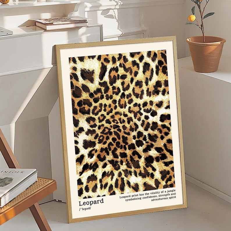 May include: Framed leopard print art. The print features a repeating pattern of brown and black spots on a tan background. The bottom of the print has the word "Leopard" and a definition. The text on the print says the print symbolizes confidence, strength, and adventurous spirit.