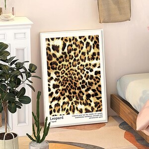 May include: A framed art print featuring a leopard print design in shades of brown and black. The print includes the word "Leopard" and text describing the print's symbolism. The artwork is displayed in a white frame.