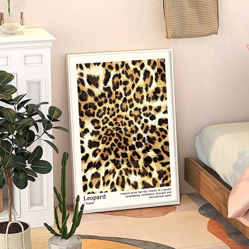 May include: A framed art print featuring a leopard print design in shades of brown and black. The print includes the word "Leopard" and text describing the print's symbolism. The artwork is displayed in a white frame.