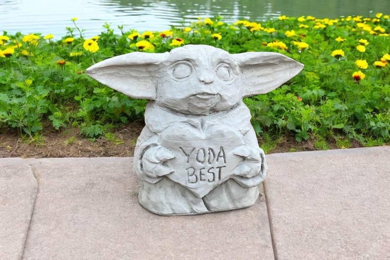 Pu&ograve; includere: Una statua di pietra grigia di un personaggio del franchise di Star Wars, che tiene un cartello a forma di cuore che dice "Yoda Best".