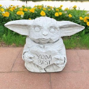 Pu&ograve; includere: Una statua di cemento grigio di un personaggio del franchise di Star Wars, che tiene un cartello a forma di cuore che dice "Yoda Best".