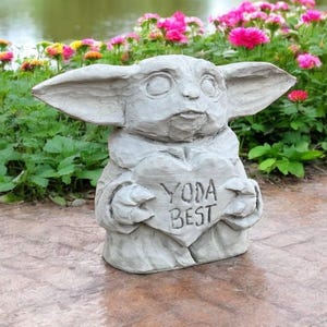 Pu&ograve; includere: Una statua di cemento grigio di un personaggio del franchise di Star Wars, che tiene un cartello a forma di cuore che dice "Yoda Best".