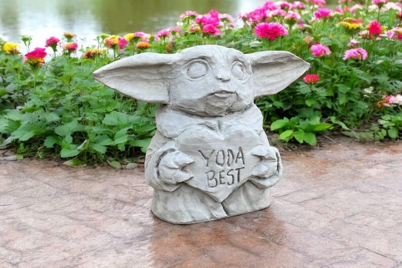 Pu&ograve; includere: Una statua di cemento grigio di un personaggio del franchise di Star Wars, che tiene un cartello a forma di cuore che dice "Yoda Best".