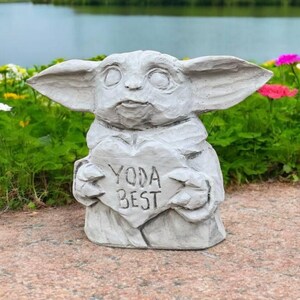Pu&ograve; includere: Una statua di cemento grigio di un personaggio del franchise di Star Wars, che tiene un cartello a forma di cuore che dice "Yoda Best".