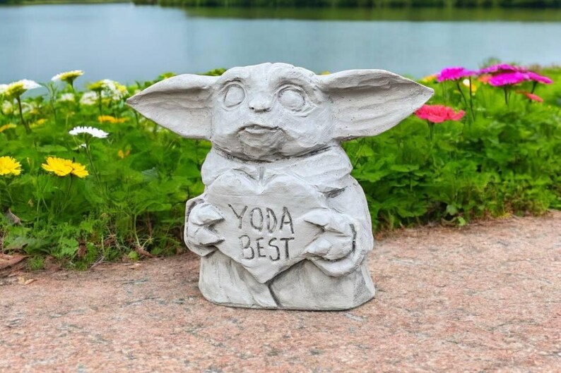 Pu&ograve; includere: Una statua di cemento grigio di un personaggio del franchise di Star Wars, che tiene un cartello a forma di cuore che dice "Yoda Best".