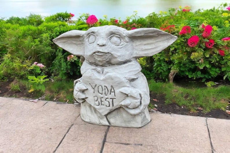 Pu&ograve; includere: Una statua di pietra grigia di un personaggio del franchise di Star Wars, che tiene un cartello a forma di cuore che dice "Yoda Best".