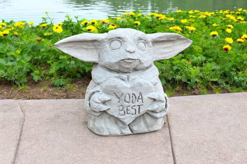 Pu&ograve; includere: Una statua di pietra grigia di un personaggio del franchise di Star Wars, che tiene un cartello a forma di cuore che dice "Yoda Best".