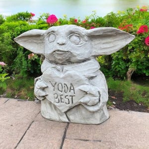 Pu&ograve; includere: Una statua di pietra grigia di un personaggio del franchise di Star Wars, che tiene un cartello a forma di cuore che dice "Yoda Best".