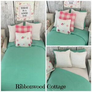May include: A doll-sized bed with a teal green duvet and white and pink patterned pillows. The pillows have embroidered flowers. The sign above the bed reads "Today is a good day".