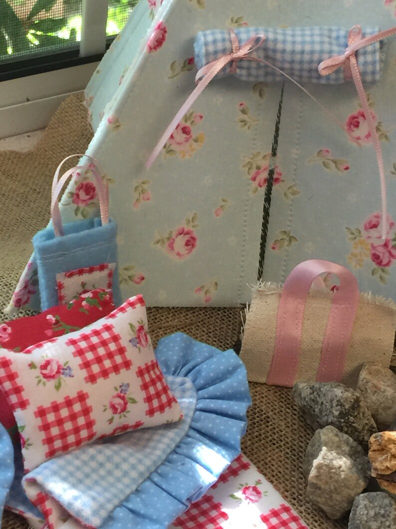 May include: A miniature blue and white gingham tent with a pink and white floral print. The tent has a small blue pillow with a red and white gingham print and a pink and white floral print. There is a small blue and white gingham blanket and a small pink and white floral print bag.