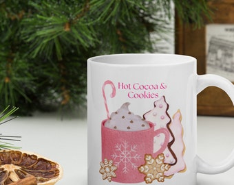 May include: White ceramic mug with a pink and white illustration of a mug of hot cocoa with whipped cream and chocolate chips, a candy cane, and cookies. The text "Hot Cocoa & Cookies" is printed in pink on the mug.