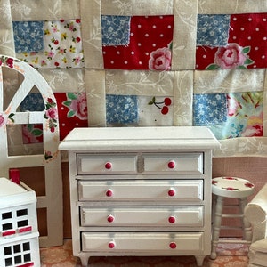 May include: White wooden dresser with four drawers and pink knobs. The dresser is sitting on a pink and white patterned floor.
