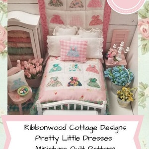 Pode incluir: Um padrão de colcha em miniatura com uma colcha rosa e branca com um desenho de pequenos vestidos. A colcha está em uma cama de boneca com uma cabeceira branca e um travesseiro rosa e branco. O padrão de colcha é intitulado "Ribbonwood Cottage Designs Pretty Little Dresses Miniature Quilt Pattern" e inclui uma opção de download PDF.