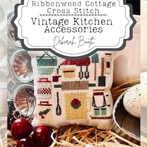 May include: A cross-stitch pillow featuring a vintage kitchen scene with red, green, and yellow details. The pillow is surrounded by decorative elements, including cherries and the text "Ribbonwood Cottage Cross Stitch Vintage Kitchen Accessories Deborah Booth."