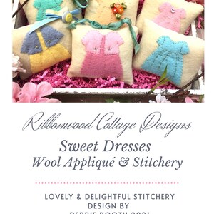 Puede incluir: Seis adornos de cojín de fieltro en una caja de regalo de papel triturado rosa. Cada cojín presenta un vestido de fieltro de color diferente con detalles bordados. Los cojines están etiquetados con "Ribbonwood Cottage Designs Sweet Dresses Wool Appliqué & Stitchery" y "Lovely & Delightful Stitchery Design by Debbie Booth 2021".