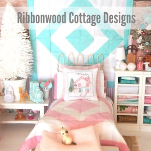 May include: A miniature dollhouse bedroom with a pink and white chevron patterned bedspread, a white pillow with a winter scene embroidered on it, and a white Christmas tree in the corner. The room is decorated with a turquoise and white quilt on the wall and a white shelf with miniature items.