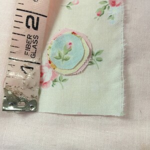 Op de afbeelding: Een close-up van een stuk stof met een bloemenpatroon en een gelaagde stofbloem applicatie in tinten roze, geel en blauw.