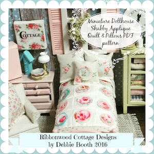 Op de afbeelding: Een miniatuur poppenhuis slaapkamer met een wit dekbed en kussens met bloemmotieven. Het dekbed heeft een roze, blauwe en witte kleurstelling. De kussens zijn wit met roze en blauwe bloemmotieven. Het bed is van hout en heeft een roze hoofdeinde. De kamer is versierd met een roze en witte bloemenbehang. De tekst "Miniature Dollhouse Shabby Applique Quilt & Pillows PDF pattern" is zichtbaar in de afbeelding. De tekst "Ribbonwood Cottage Designs by Debbie Booth 2016" is ook zichtbaar in de afbeelding.