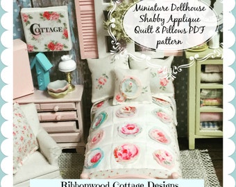 Op de afbeelding: Een miniatuur poppenhuis slaapkamer met een wit dekbed en kussens met bloemmotieven. Het dekbed heeft een roze, blauwe en witte kleurstelling. De kussens zijn wit met roze en blauwe bloemmotieven. Het bed is van hout en heeft een roze hoofdeinde. De kamer is versierd met een roze en witte bloemenbehang. De tekst "Miniature Dollhouse Shabby Applique Quilt & Pillows PDF pattern" is zichtbaar in de afbeelding. De tekst "Ribbonwood Cottage Designs by Debbie Booth 2016" is ook zichtbaar in de afbeelding.