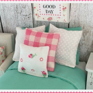 May include: A bed with a teal green duvet cover and three pillows. The pillows are white with pink and white gingham, white with white polka dots, and white with pink floral designs. The sign above the bed reads "Good Day".