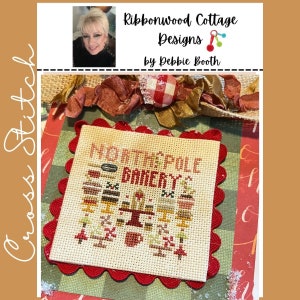 May include: Cross stitch pattern of a red and white checkered bakery with the text "North Pole Bakery" in brown and white lettering. The bakery is surrounded by a red scalloped border.