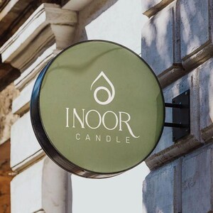 May include: A round, green sign with a black border and white text that reads "INOOR CANDLE". The sign has a stylized water drop design with a circle inside.