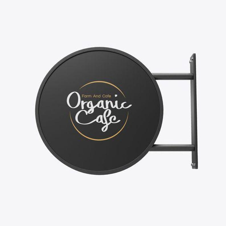 May include: Black round sign with a gold circle and white text that reads "Farm And Cafe Organic Cafe". The sign is attached to a black metal frame.