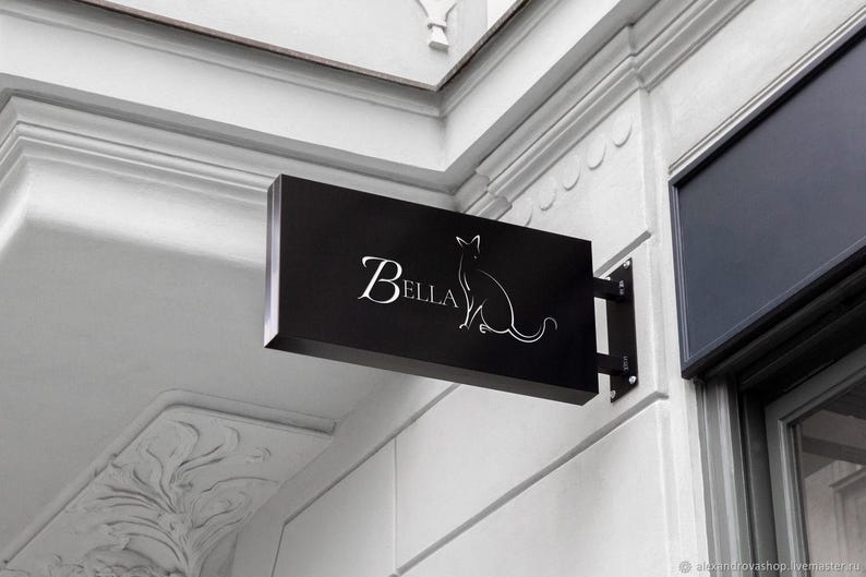 May include: A black sign with white lettering and a silhouette of a cat. The sign reads "Bella".