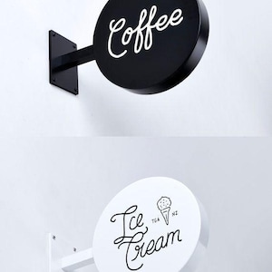 May include: Two round, black and white signs with metal brackets. The black sign says "Coffee" in white cursive writing. The white sign says "Ice Cream" in black cursive writing with a small black and white ice cream cone graphic.
