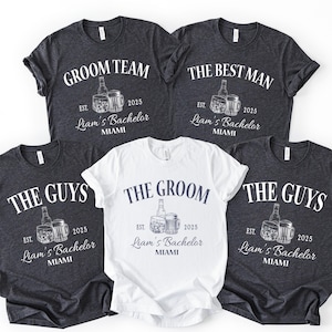 Może przedstawiać: Pięć koszulek w ciemnych i białych kolorach z napisami na wieczór kawalerski. Koszulki przedstawiają napisy "Groom Team", "The Best Man", "The Guys" i "The Groom". Każda koszulka zawiera "Liam's Bachelor Miami" i rok "2025".