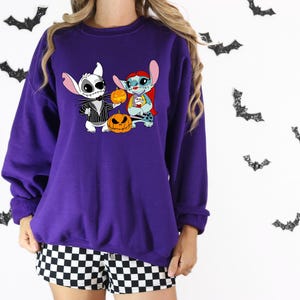 May include: A purple sweatshirt with a Halloween-themed graphic of Jack Skellington and Stitch holding pumpkins. Black bat decorations are on the background. The person is wearing black and white checkered shorts.