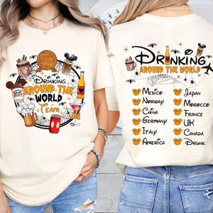 May include: Cream-colored t-shirt with a graphic featuring the text "DRINKING AROUND THE WORLD TEAM." The design includes cartoon beverages and a globe. The back of the shirt lists countries with Mickey Mouse heads.