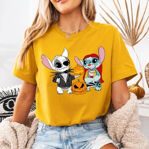 May include: Mustard yellow t-shirt with a Halloween graphic. The graphic shows two cartoon characters, one like Jack Skellington and the other Stitch, holding pumpkins. The Jack Skellington character is in a black and white striped suit.